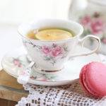 Englisches Teeservice aus Porzellan mit Kamelienblütenmuster, bestehend aus einer zarten Teetasse auf Spitze mit einem rosa Macaron.